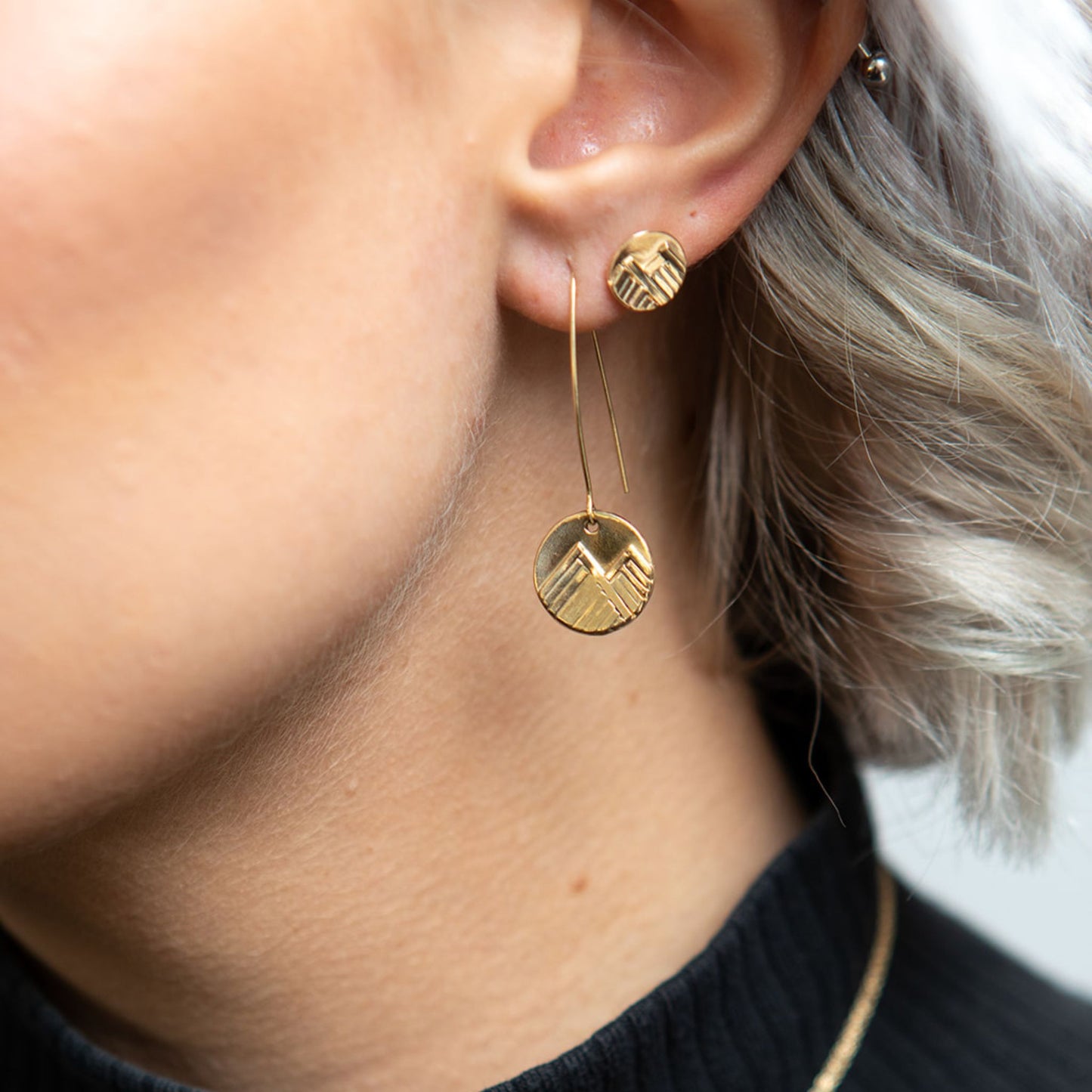 Closeup of model wearing gold mountain love stud earrings