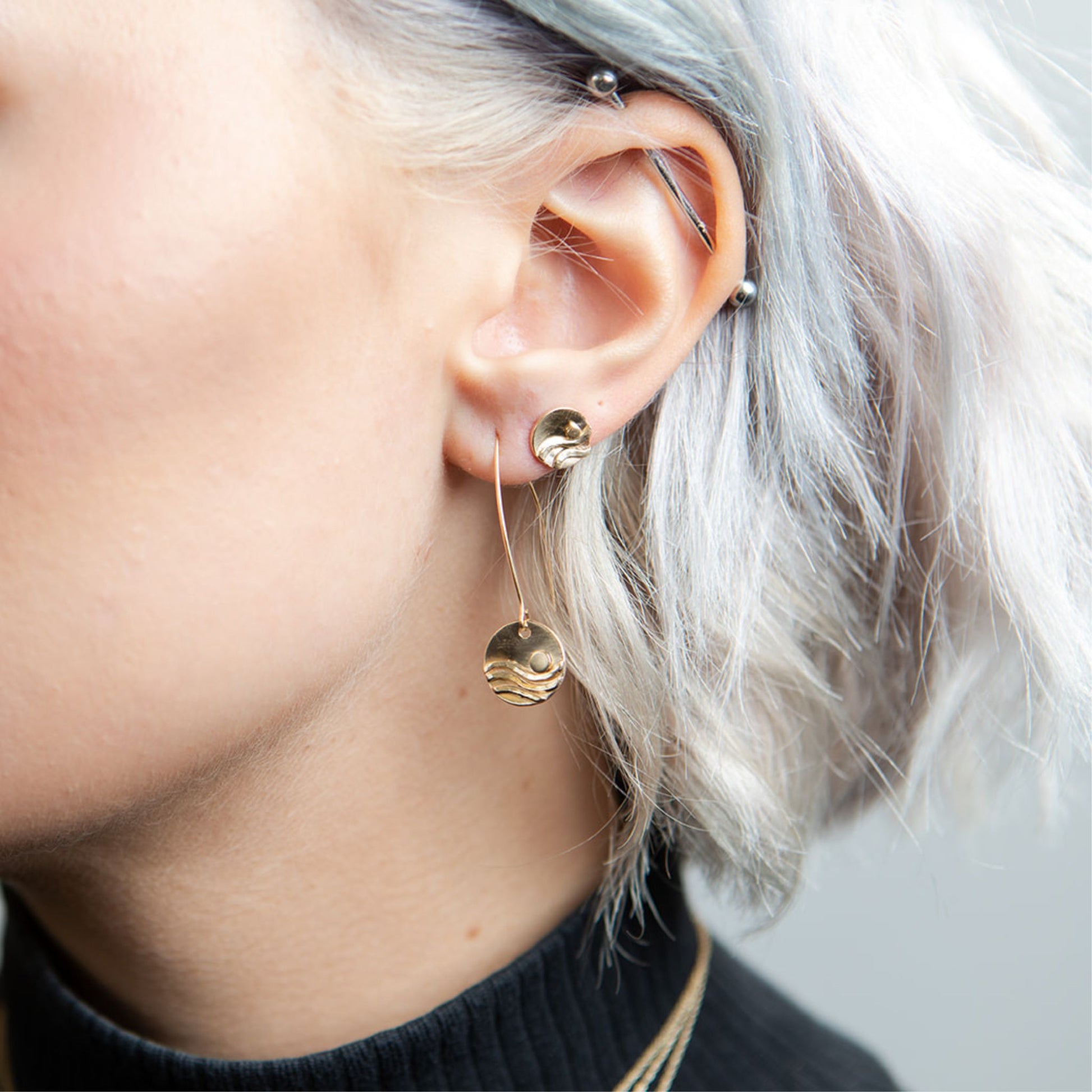 Closeup of model wearing gold reflections wave stud earrings
